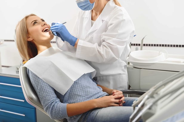 Woman receiving dental treatment with cuspidor next to dental chair
